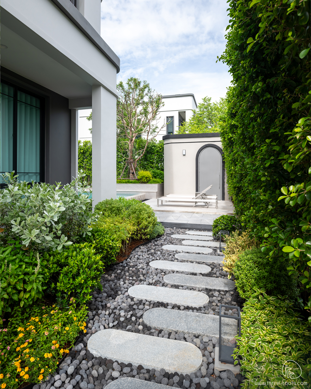 ออกแบบสวน จัดสวน ครบวงจร
มุมทางเดินเข้าใช้งานสวนจากหน้าบ้านไปข้างบ้าน
มีพุ่มพรรณไม้ที่ไล่โทนสีมองแล้วรู้สึกผ่อนคลาย
ทางเดินที่ใช้หินก่อนใหญ่ และแผ่นทางเดินแบบโค้งมนดูสบายตา
บริษัททรีรูท ออกแบบสวน